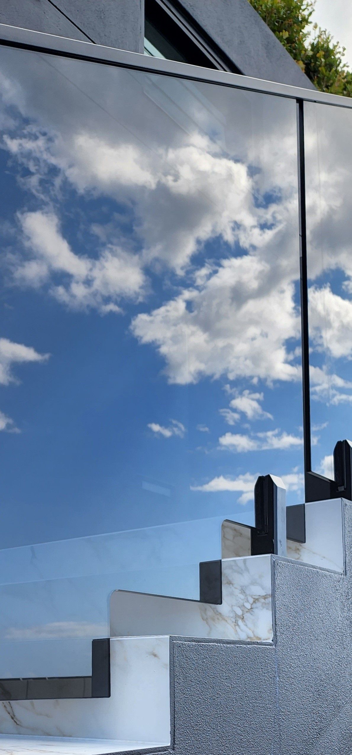 A modern building reflecting a blue sky with clouds; steps made of stone in various colors ascend.