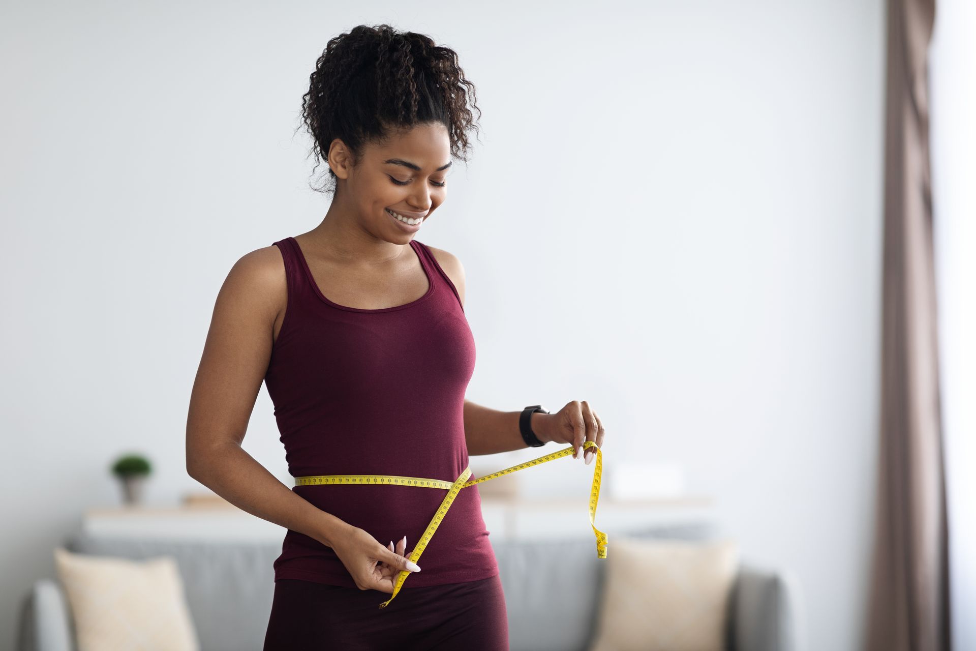 A woman is measuring her waist with a tape measure.