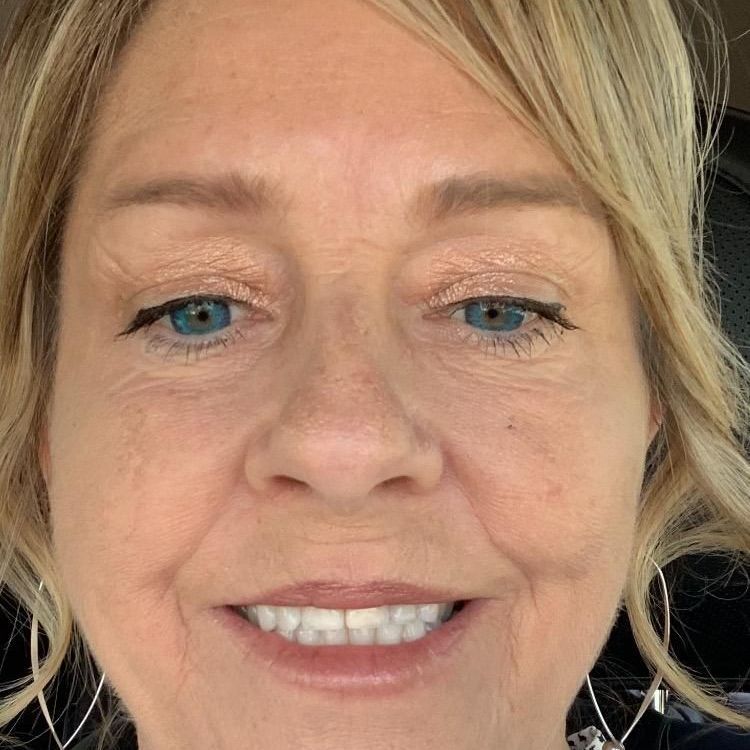 A close up of a woman 's face smiling and wearing a necklace.