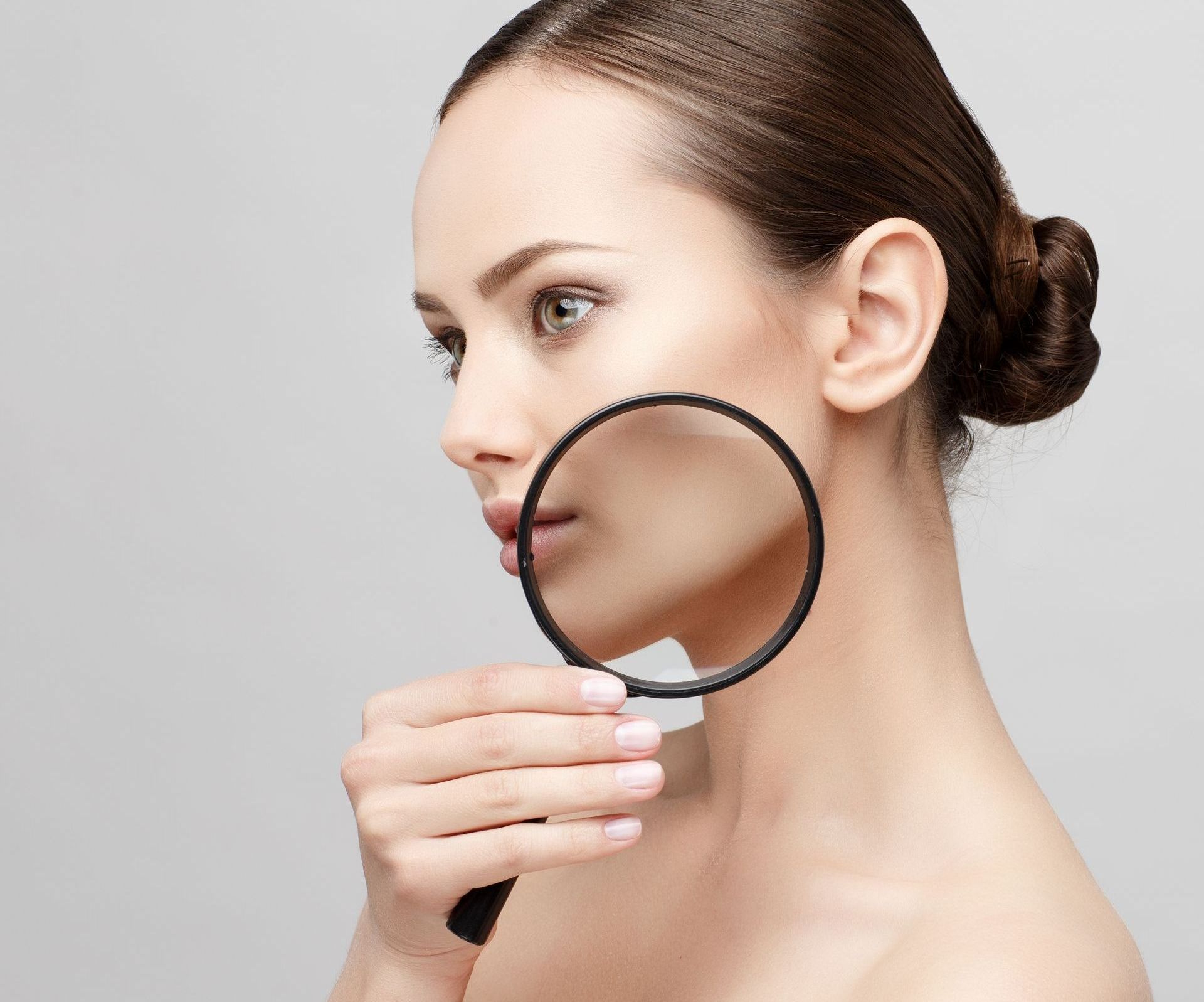 A woman is looking through a magnifying glass at her face.