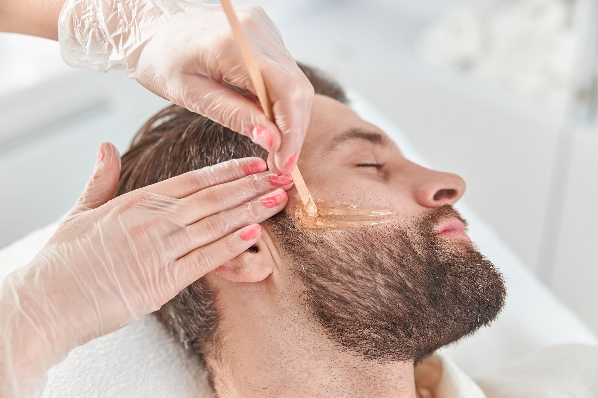 A man with a beard is getting a wax treatment on his face.