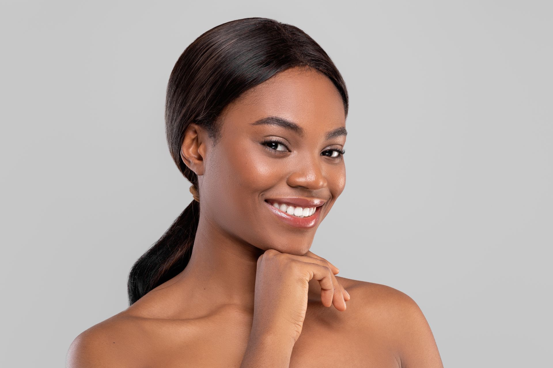 A woman is smiling and touching her face with her hand.