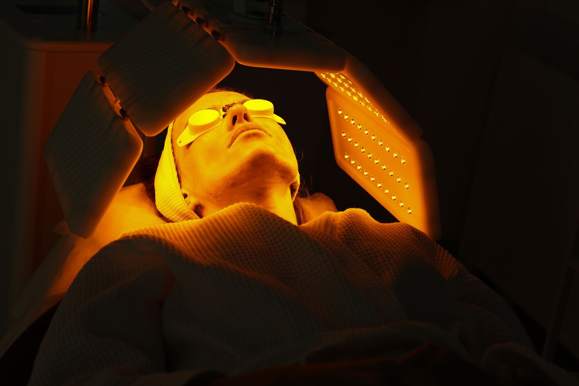 A woman is getting a facial treatment with a yellow light on her face.