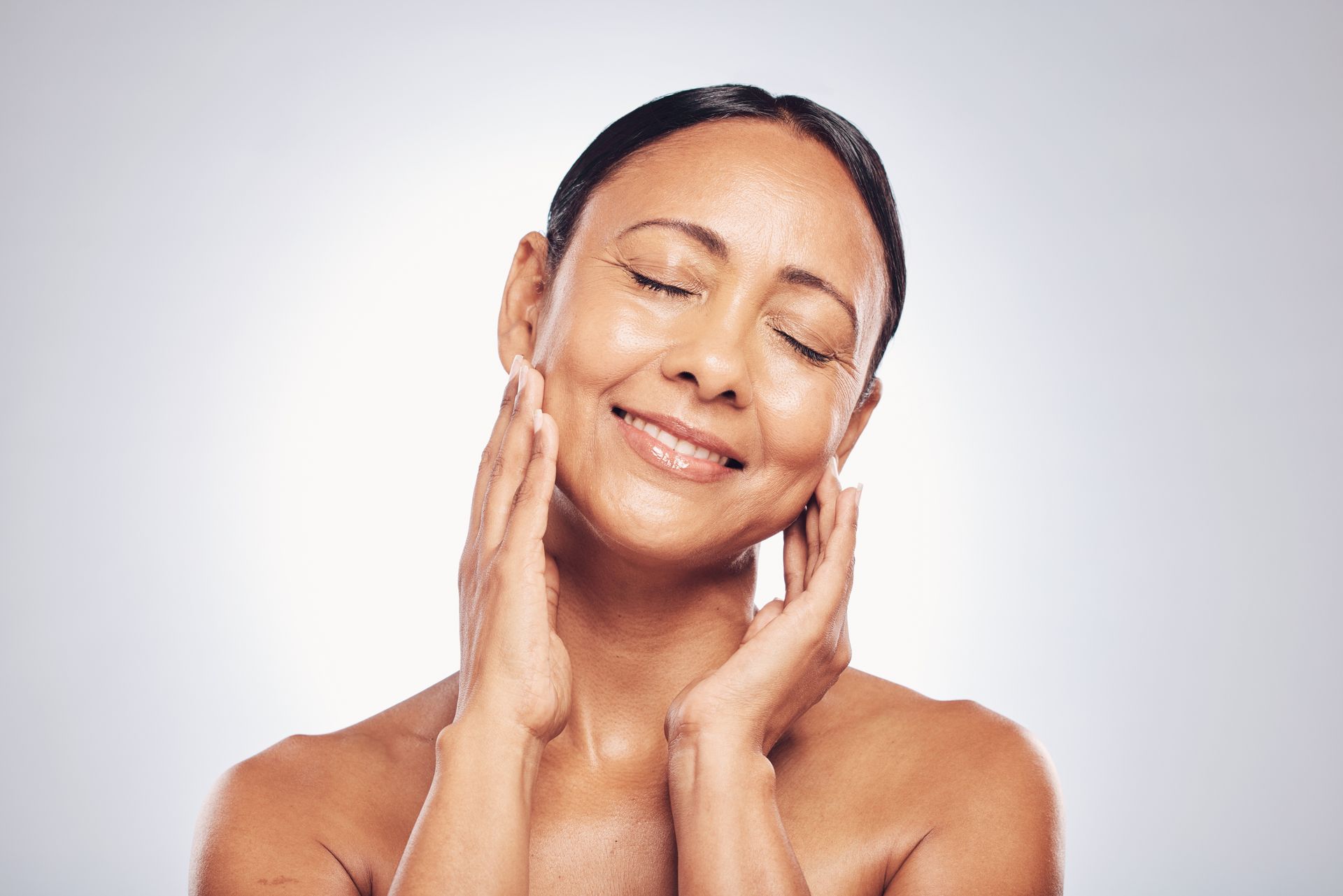 A woman is smiling and touching her face with her hands.