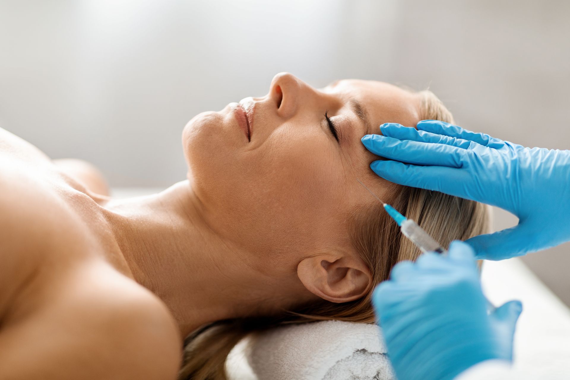 A woman is getting a botox injection in her forehead.