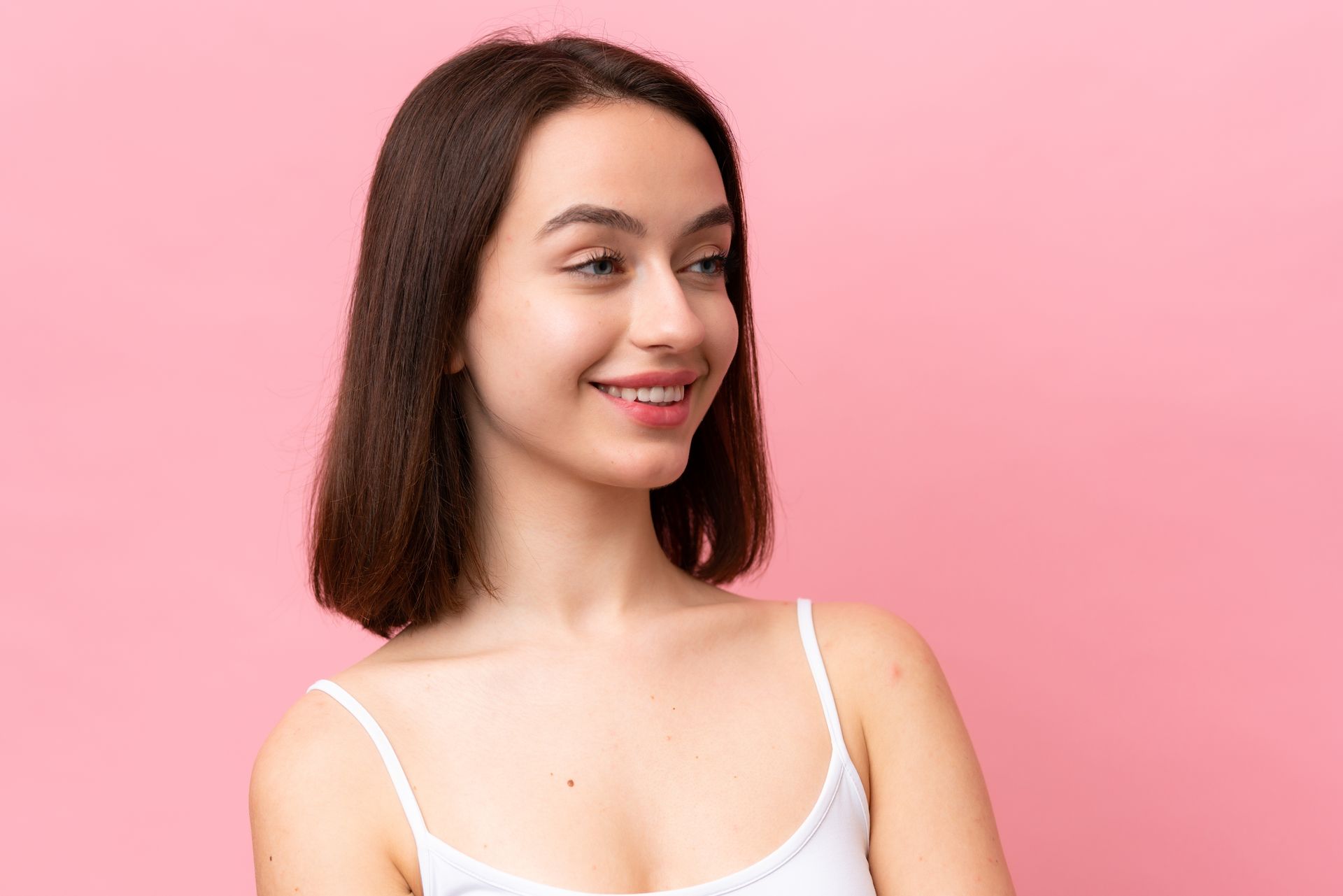 A young woman is smiling and looking to the side over a pink background.