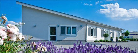 Ein weißes Haus mit lila Blumen davor.