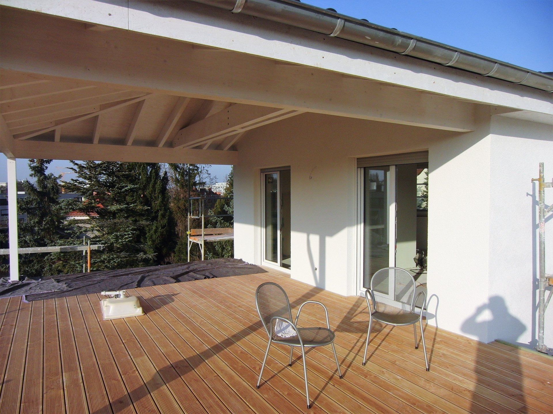 Eine Holzterrasse mit Stühlen und ein weißes Gebäude im Hintergrund
