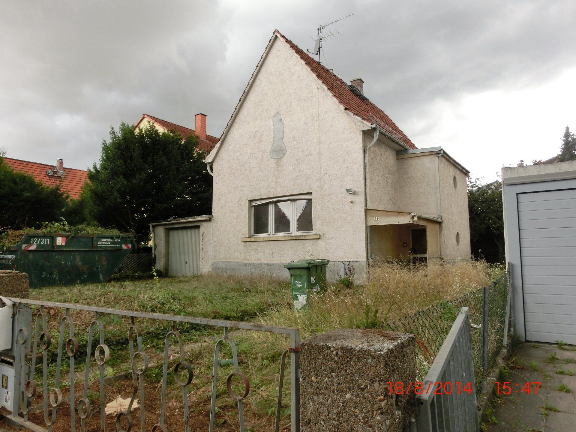 Ein weißes Haus mit einer grünen Mülltonne davor