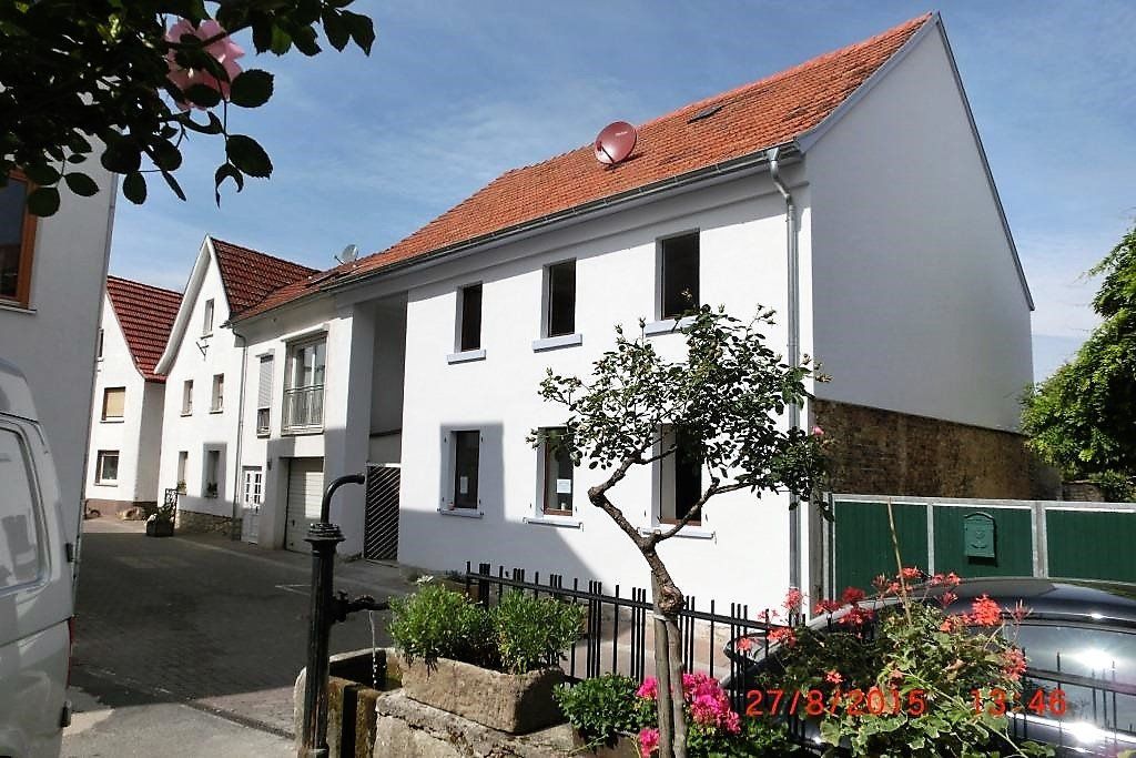 Ein weißes Haus mit einem roten Ziegeldach ist von einem grünen Zaun umgeben