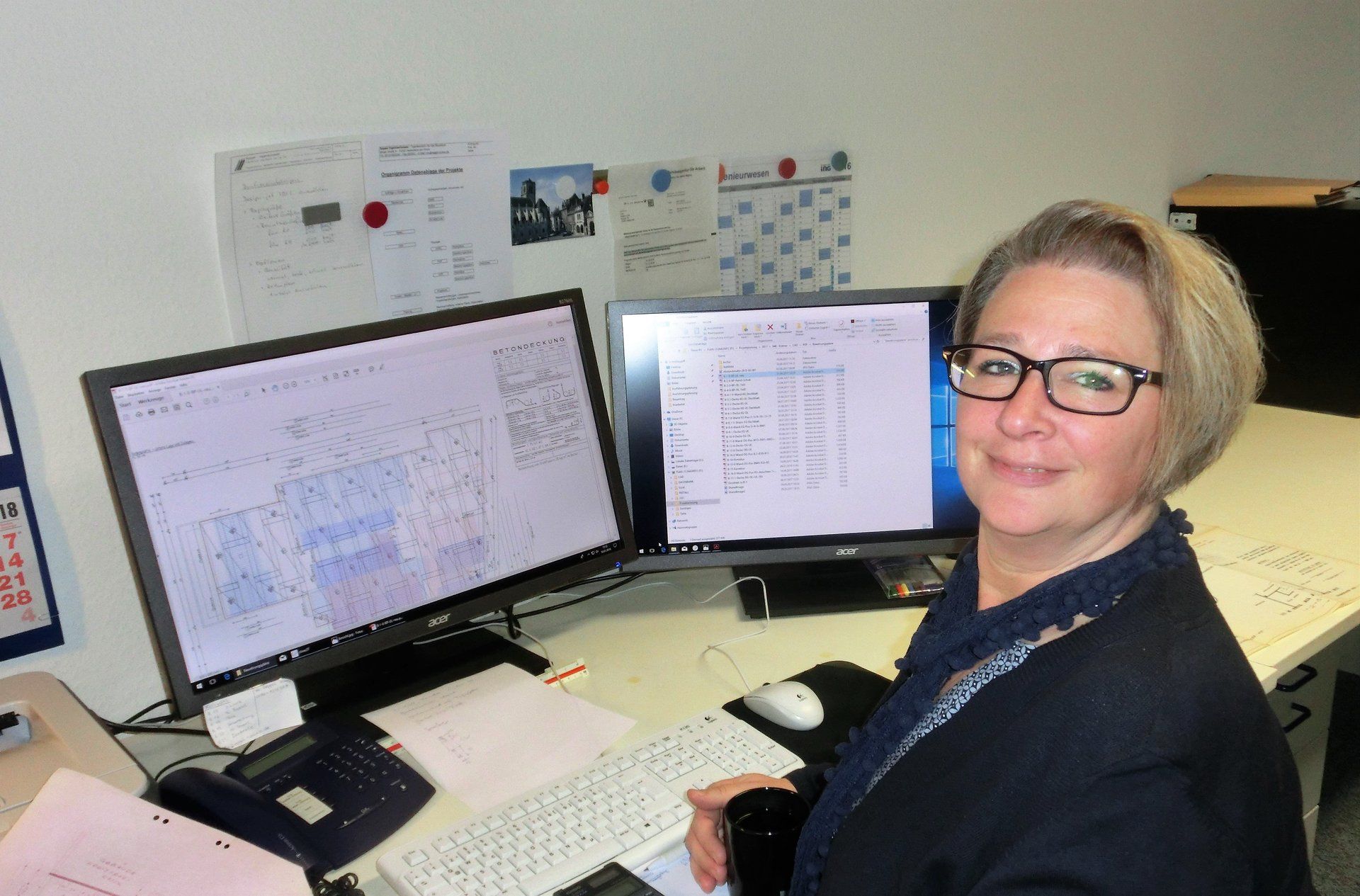 Eine Frau sitzt an einem Schreibtisch vor zwei Computerbildschirmen.