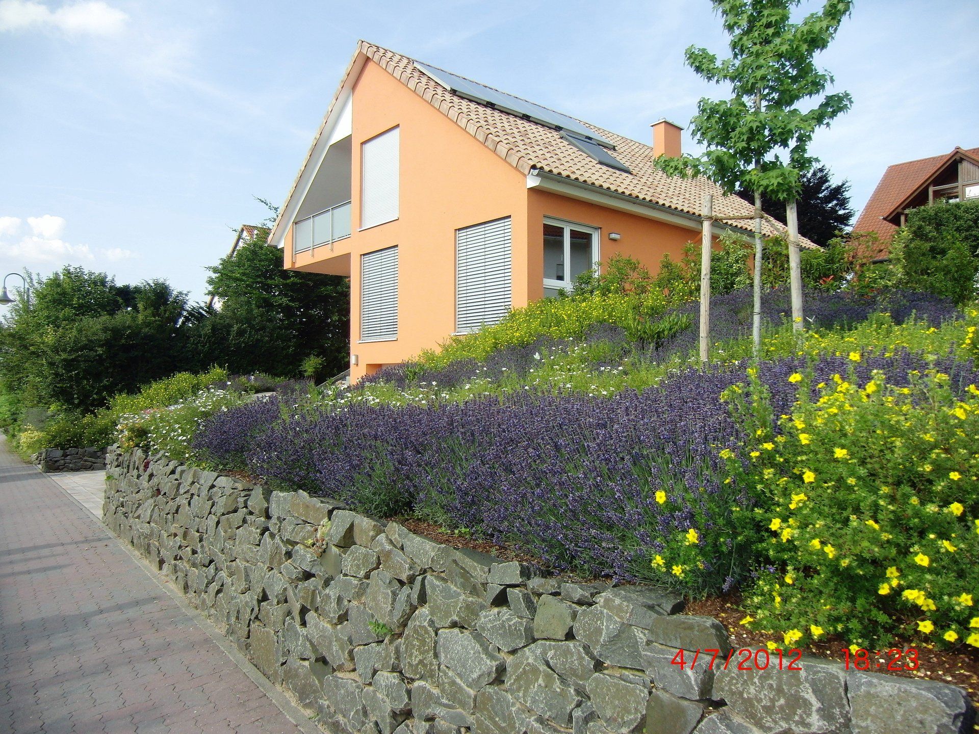 Ein orangefarbenes Haus steht auf einem Hügel, umgeben von Blumen