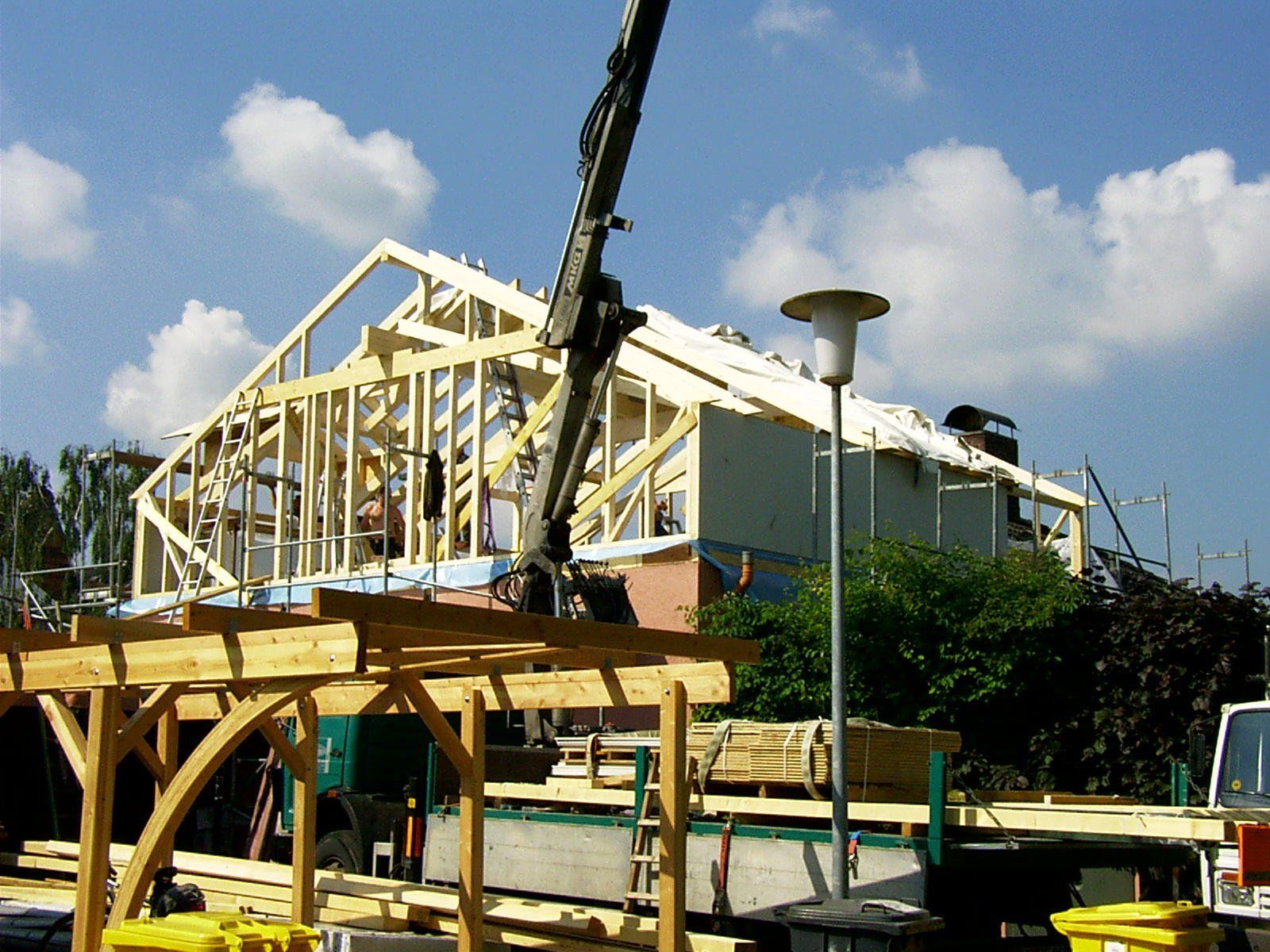 Ein Kran hebt eine Holzkonstruktion vor einem im Bau befindlichen Haus an