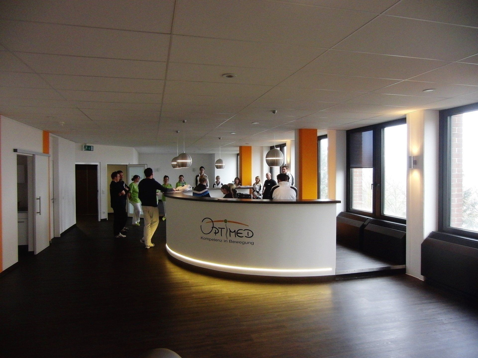 Eine Gruppe von Menschen steht um einen Empfangstresen herum, auf dem Optimo steht