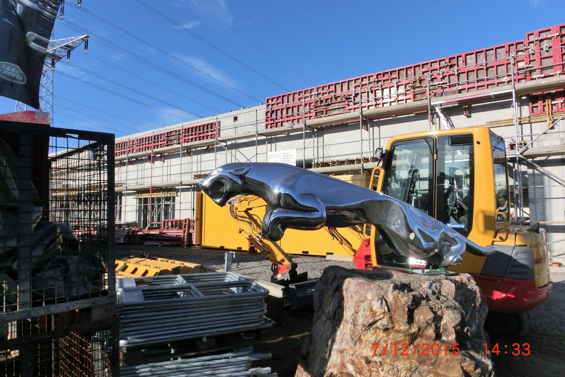 Eine Statue eines Jaguars sitzt auf einem Felsen vor einem Baufahrzeug