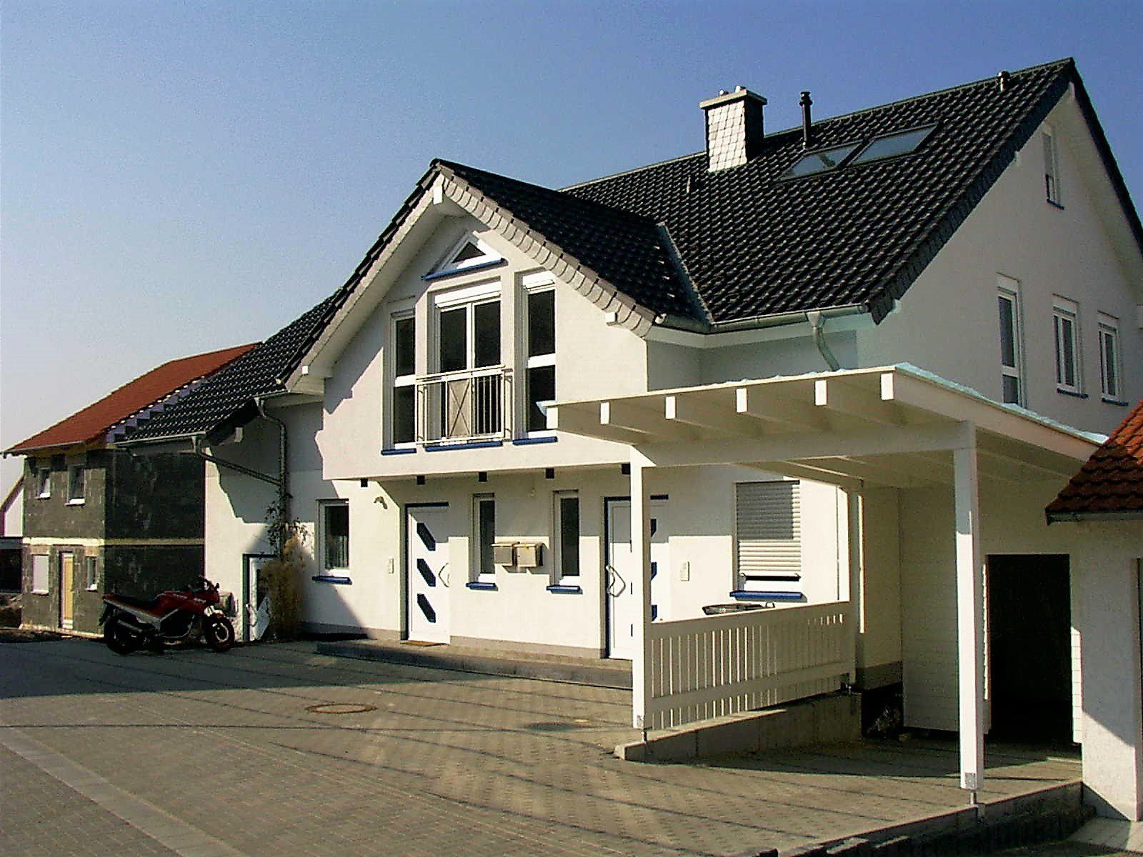 Ein weißes Haus mit schwarzem Dach und einem Carport