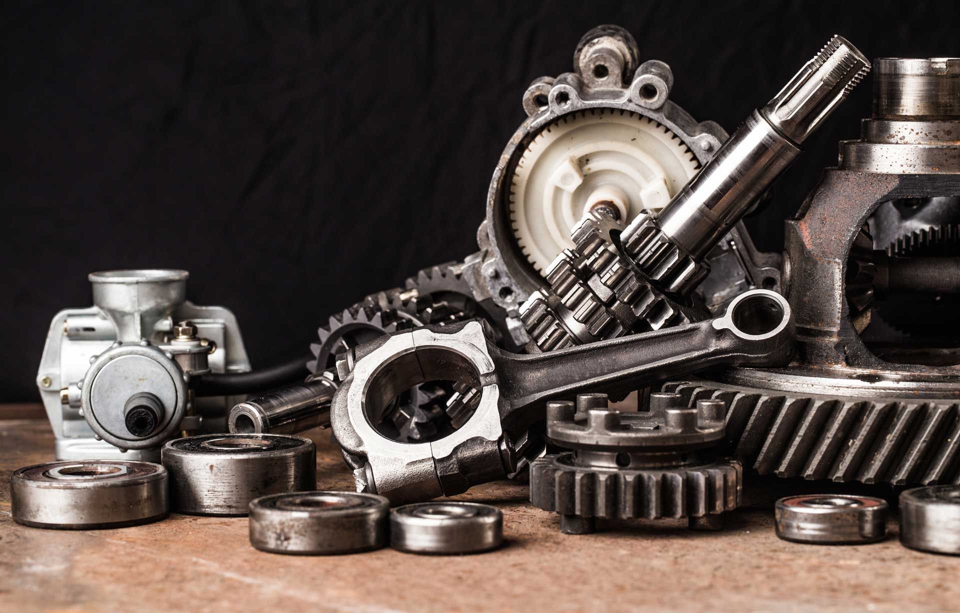Pile of various metallic car parts, including gears, bearings, and shafts, on a rough wooden surface.