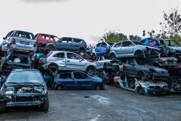 Stacks of car bodies without wheels and windshields are piled up in a salvage yard.