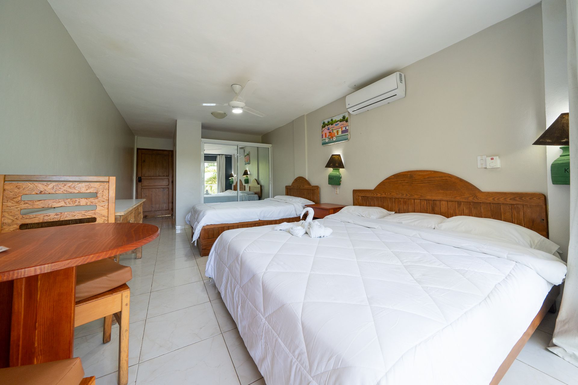 Bright bedroom with two beds, tiled floor, a desk, and a wall-mounted air conditioner