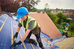 Workers installing solar panels on a rooftop, wearing blue helmets and safety vests.