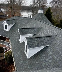 Gray-shingled house roof with a small dormer window against a blue sky