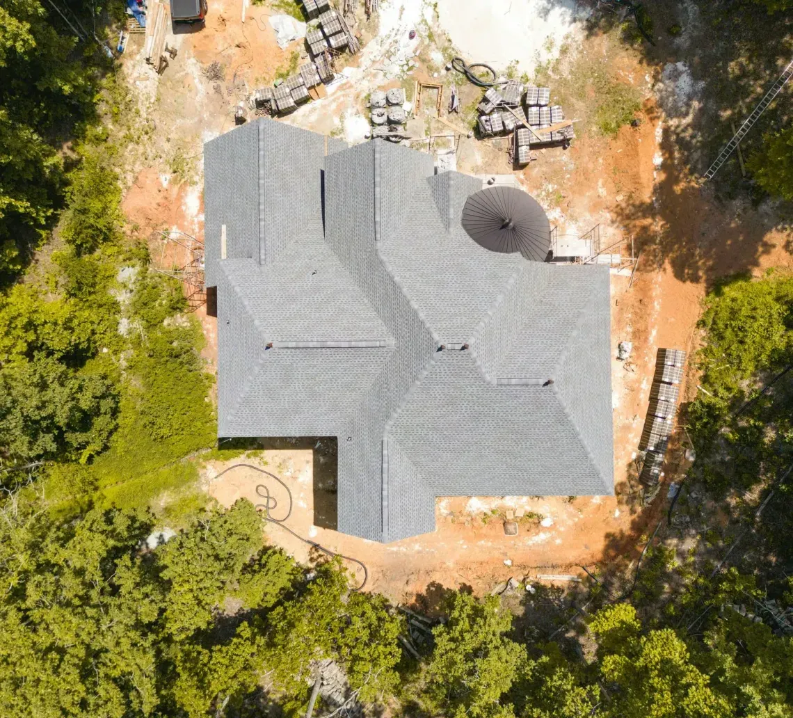 Aerial view of a gray-roofed house surrounded by trees and construction materials