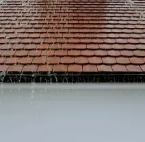 Rainwater dripping from a red-tiled roof onto a white wall
