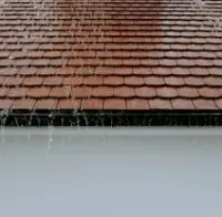 Rainwater dripping from a red-tiled roof onto a white wall