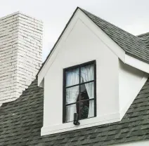 White house roof with dormer window and a brick chimney against the sky