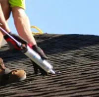 Worker applying sealant to a shingled roof with a caulking gun