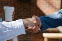 Two people in white and blue shirts shaking hands, with a coffee cup in the background.