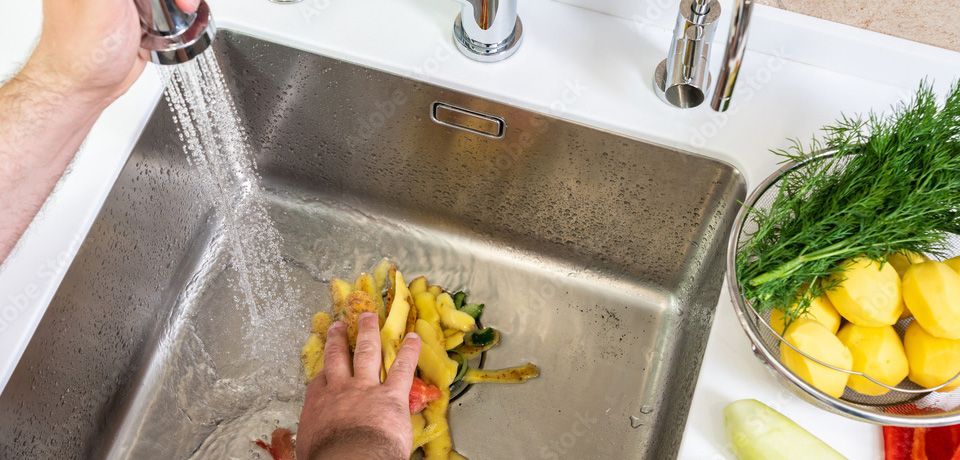 A person is washing vegetables in a stainless steel sink.