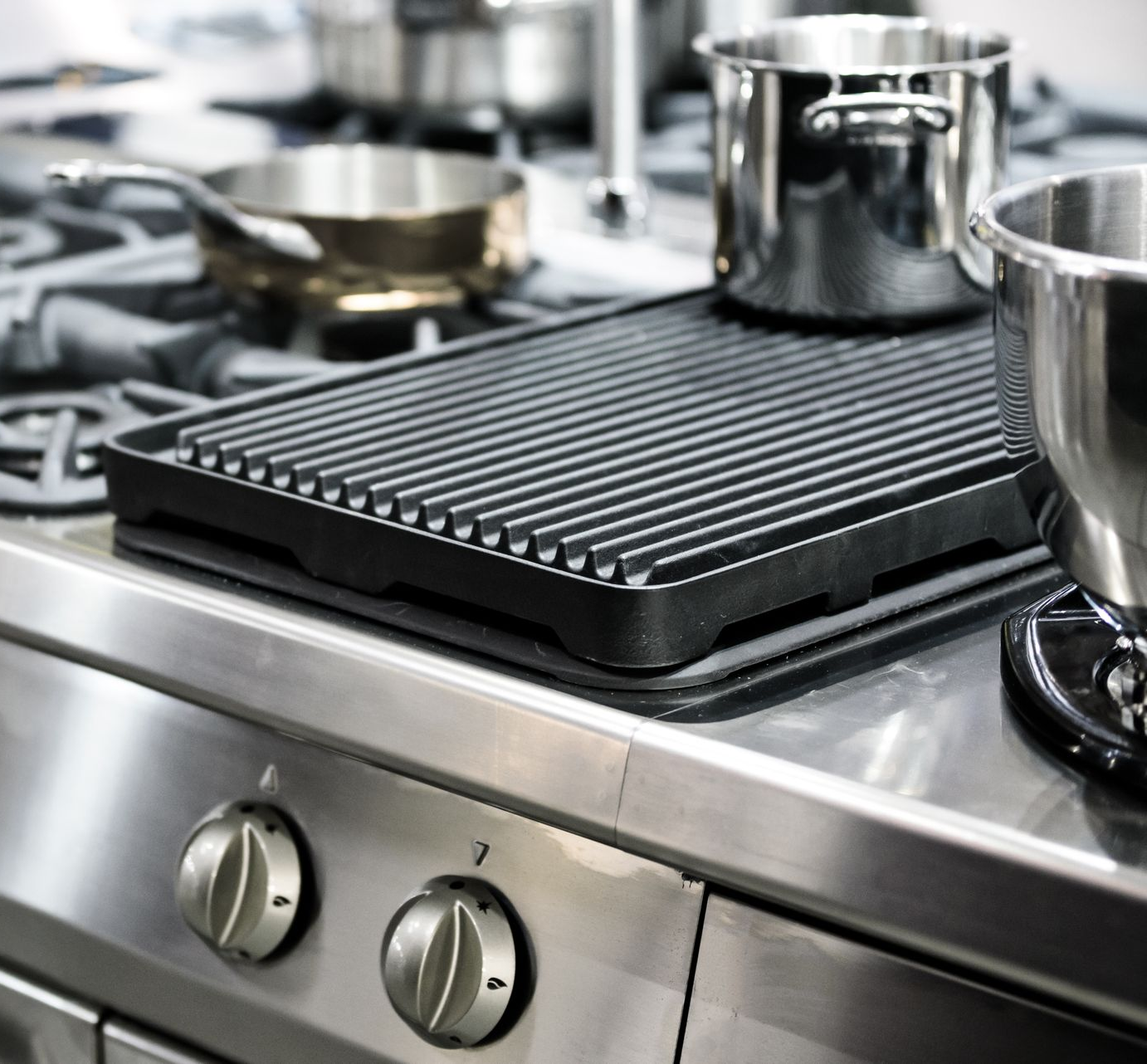 Stainless steel kitchen with pots, grill pan, and stove knobs.