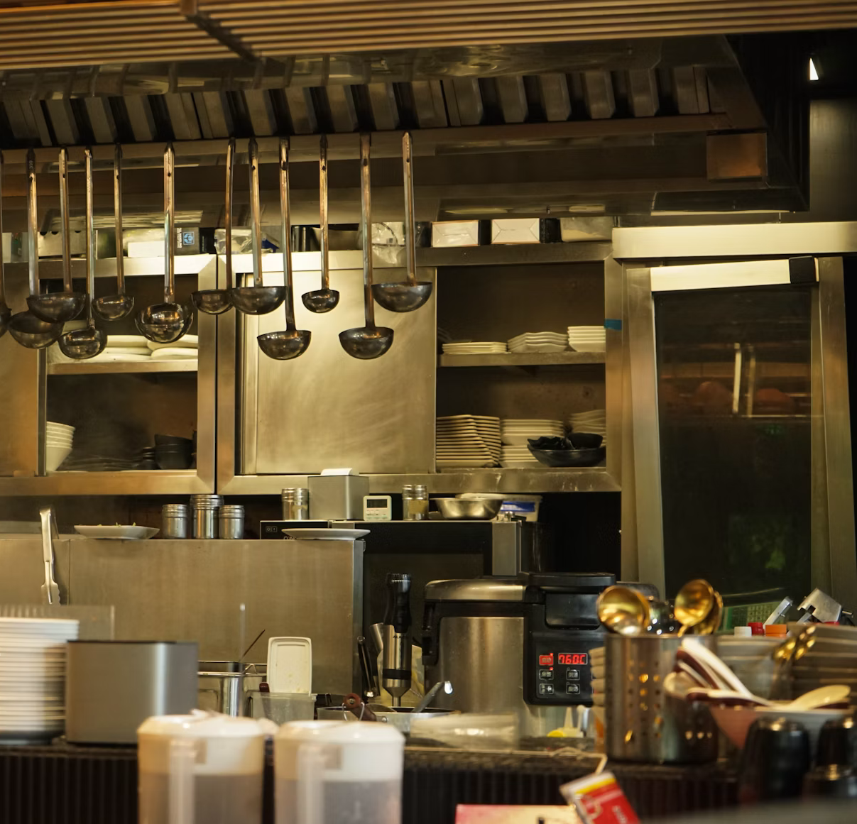 Restaurant kitchen interior with stainless steel appliances, ladles, and food prep areas.