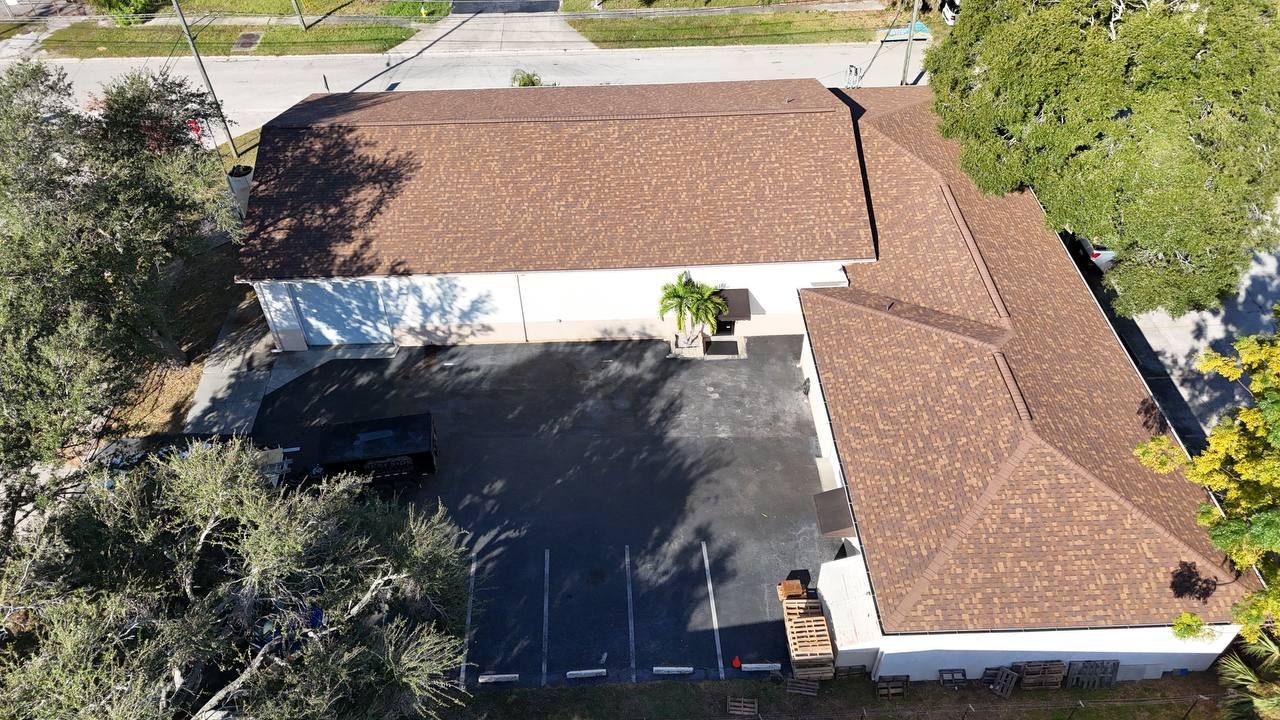 Aerial view of a one-story building with a brown roof and a black paved parking area.