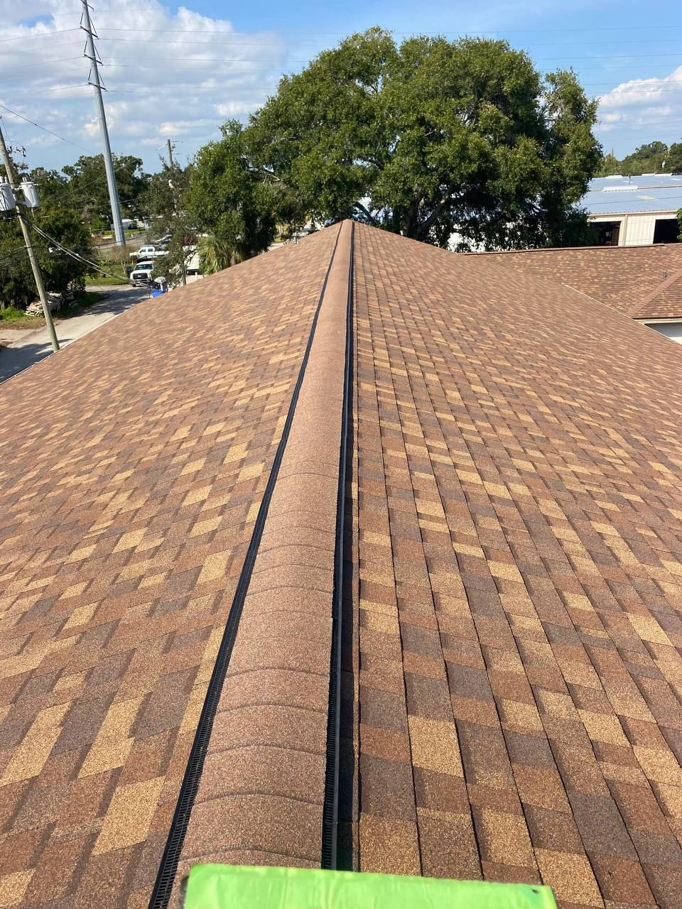 Newly shingled roof with a central ridge. Brown and tan shingles, blue sky background.