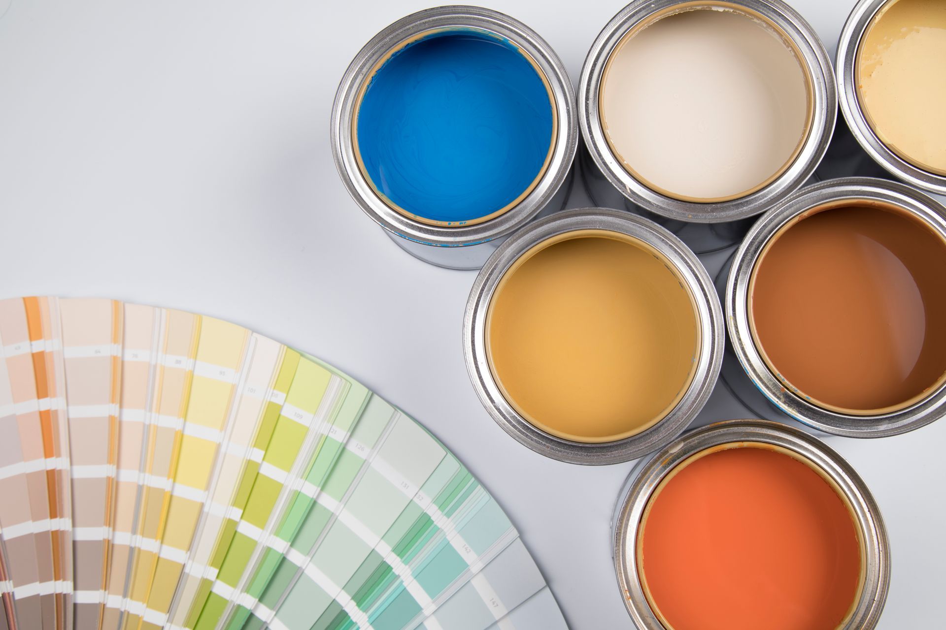 Barattoli di vernice di vari colori con un ventaglio di campioni di colore su una superficie bianca.