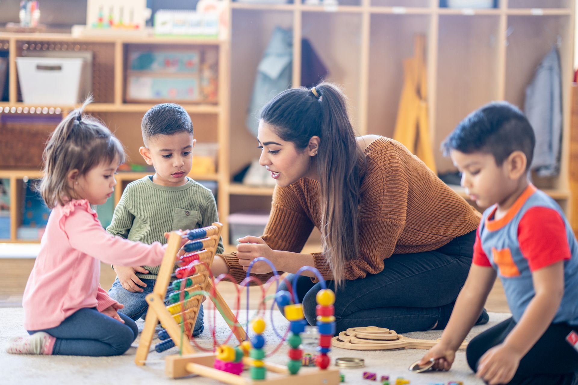 A teacher sits on the floor with students as they play with toys, part of the childcare program.