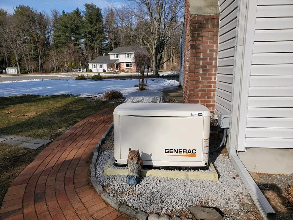 A Generac home generator is next to a brick-paved walkway and a house on a partly snowy day.