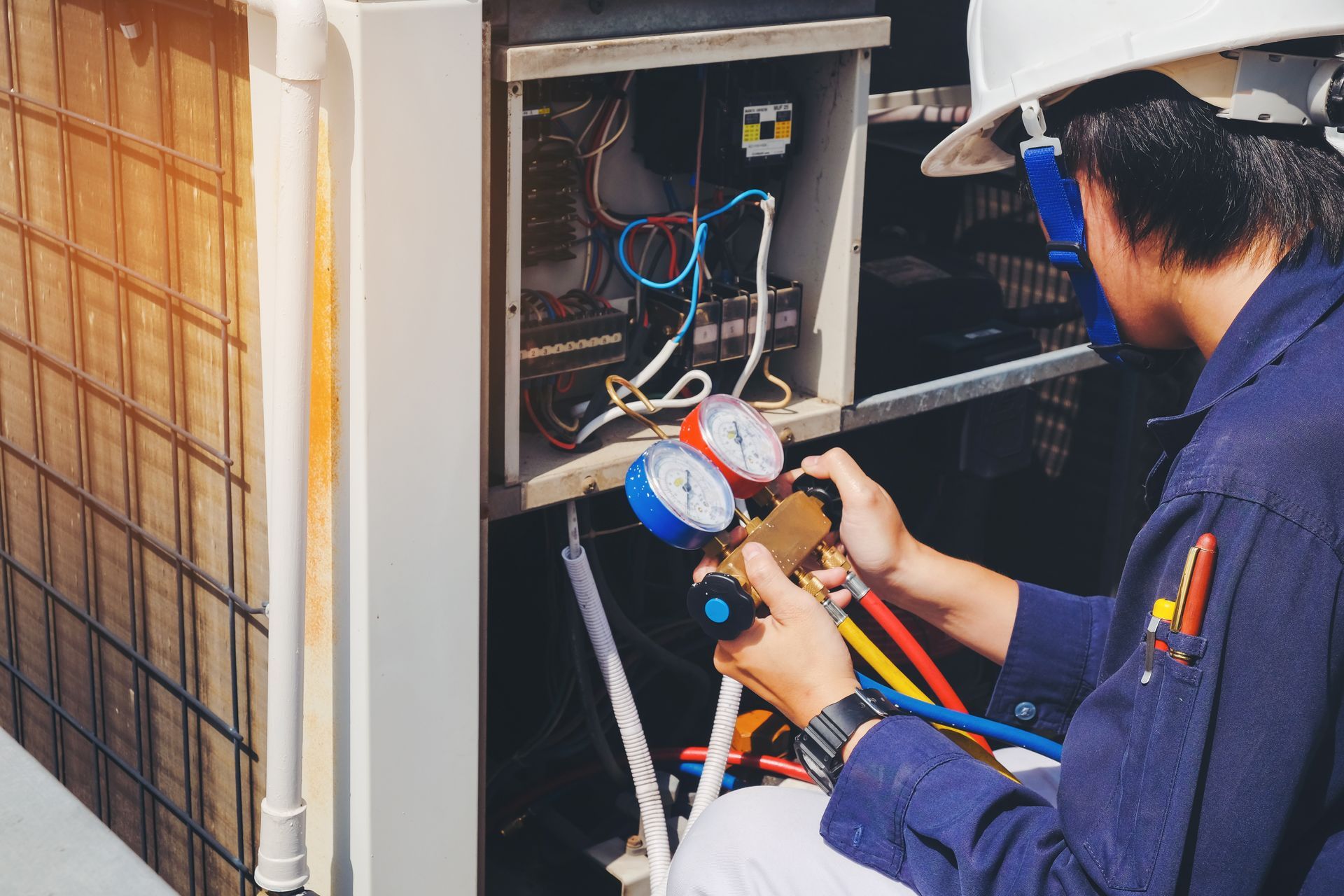 HVAC technician repairing an air conditioning unit; using gauges on colored hoses.