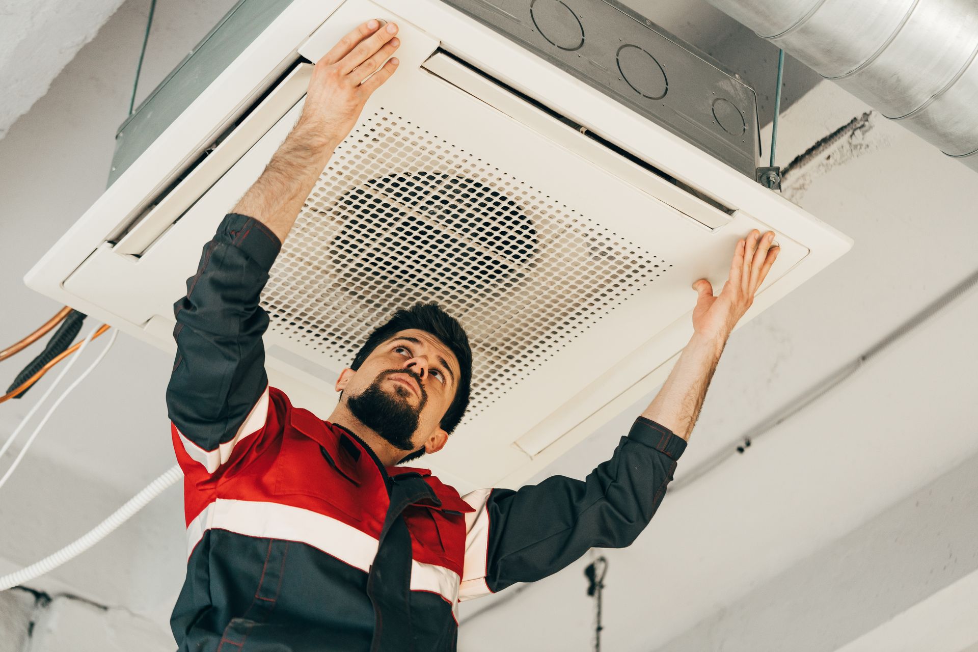Man in work uniform installing a ceiling air conditioner unit.