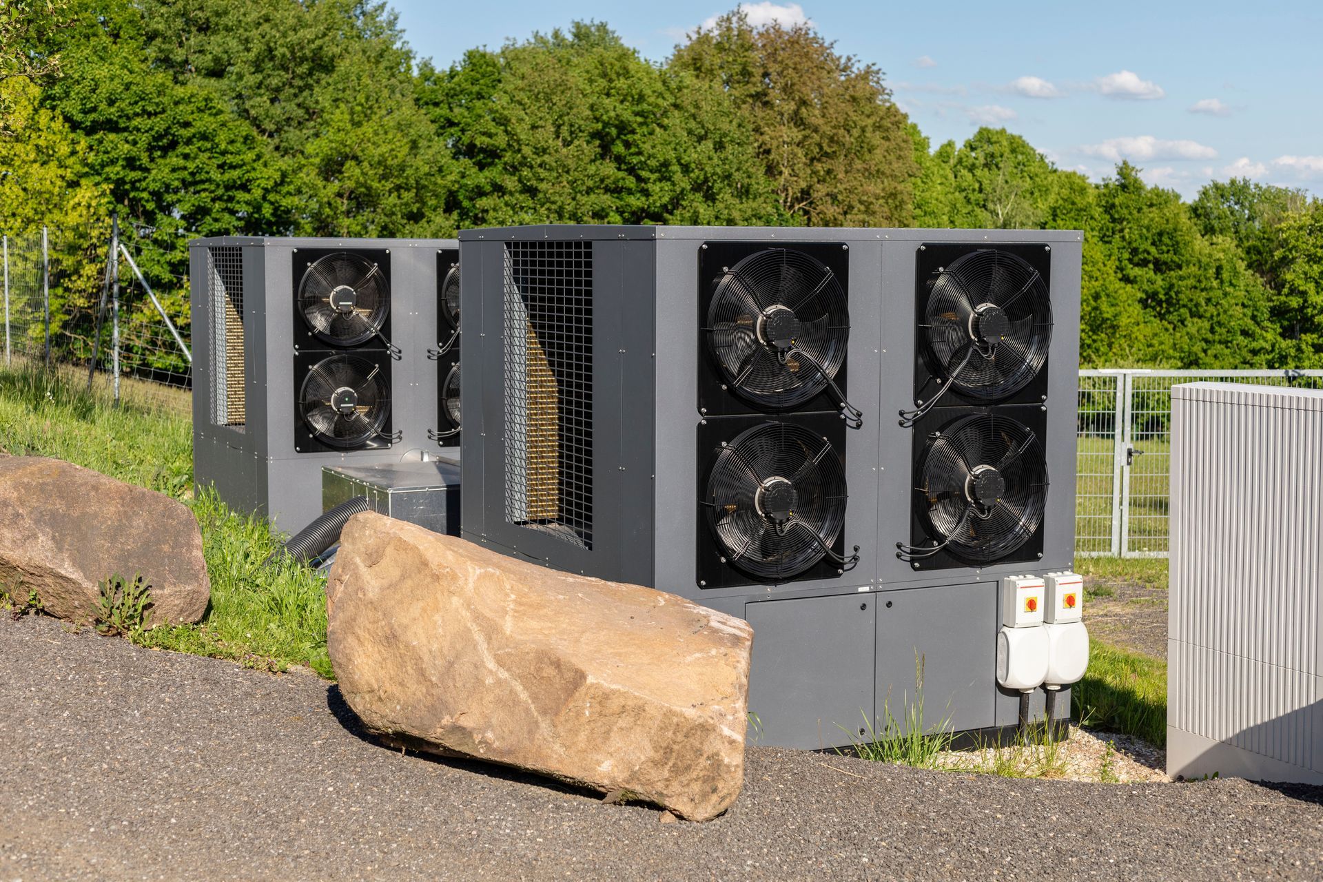 Large gray industrial units with fans outdoors, near a rock and trees.