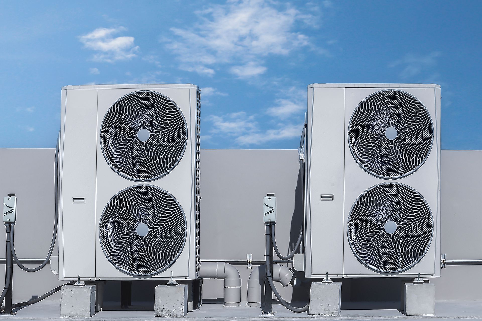 Two air conditioning units on a rooftop against a blue sky with clouds.