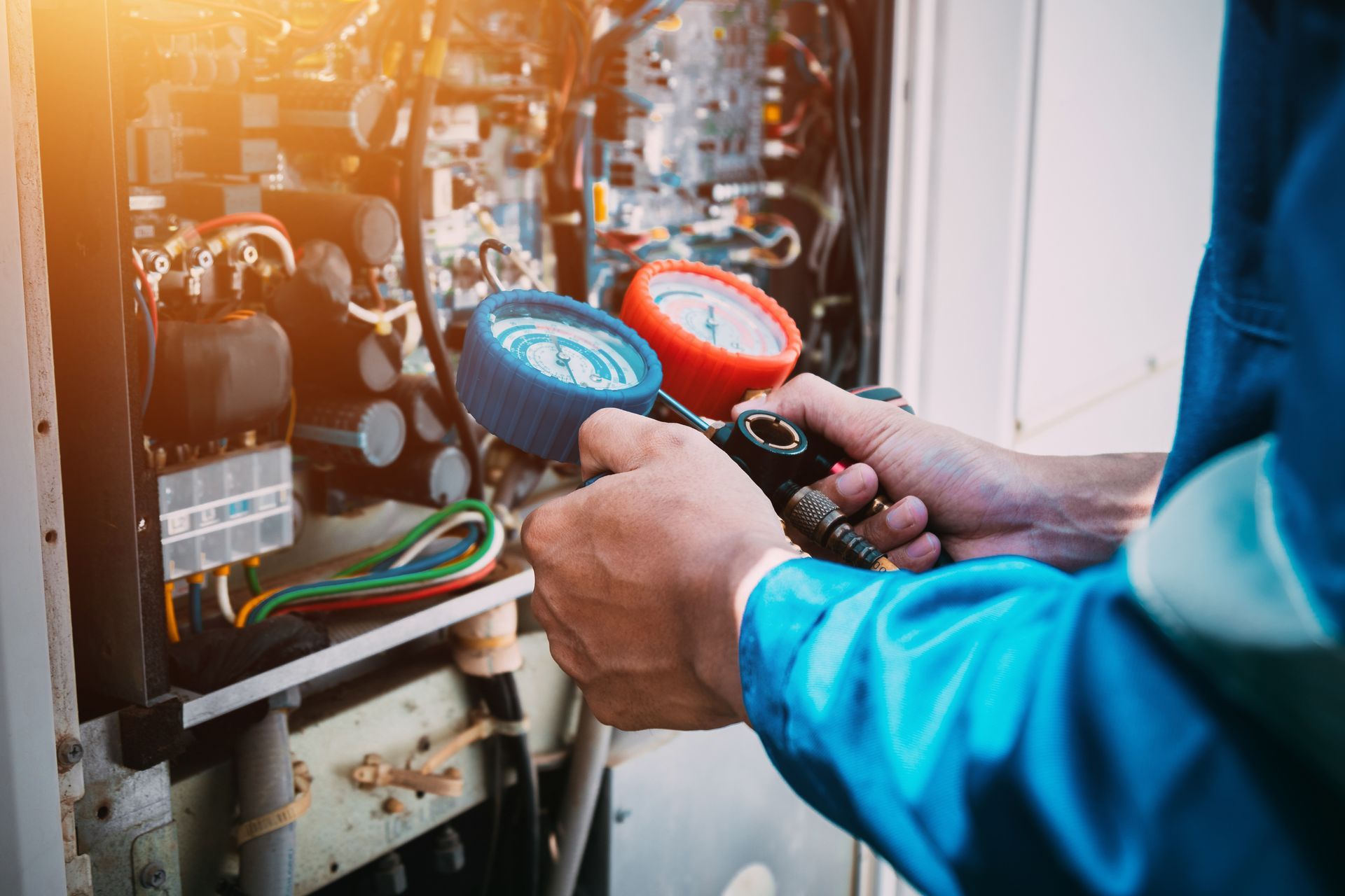 HVAC technician using gauges to inspect heating system. Blue and red gauges, equipment visible.
