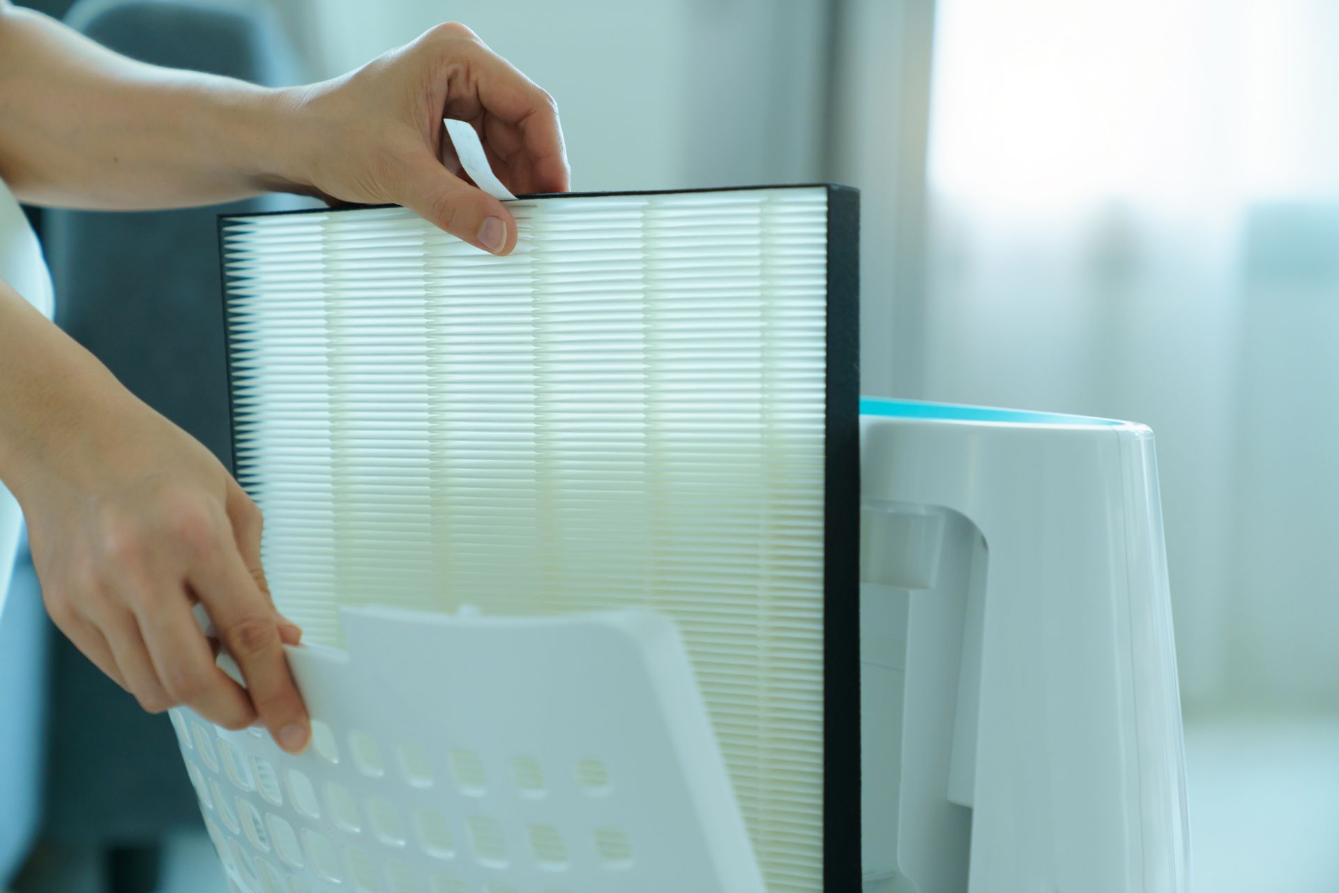 Hands removing an air purifier filter. White filter and device, bright setting.