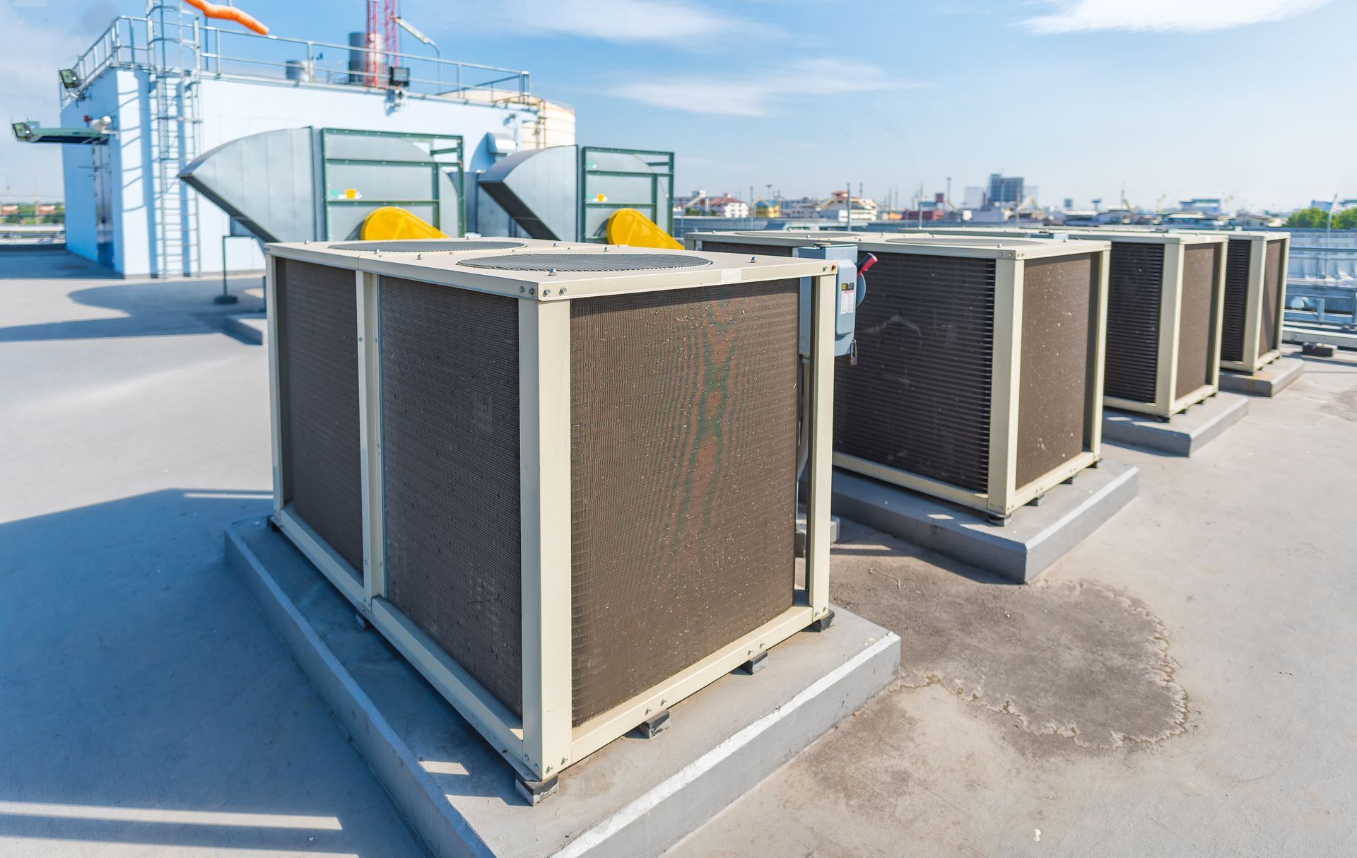 Rooftop air conditioning units lined up on a building under a bright blue sky.