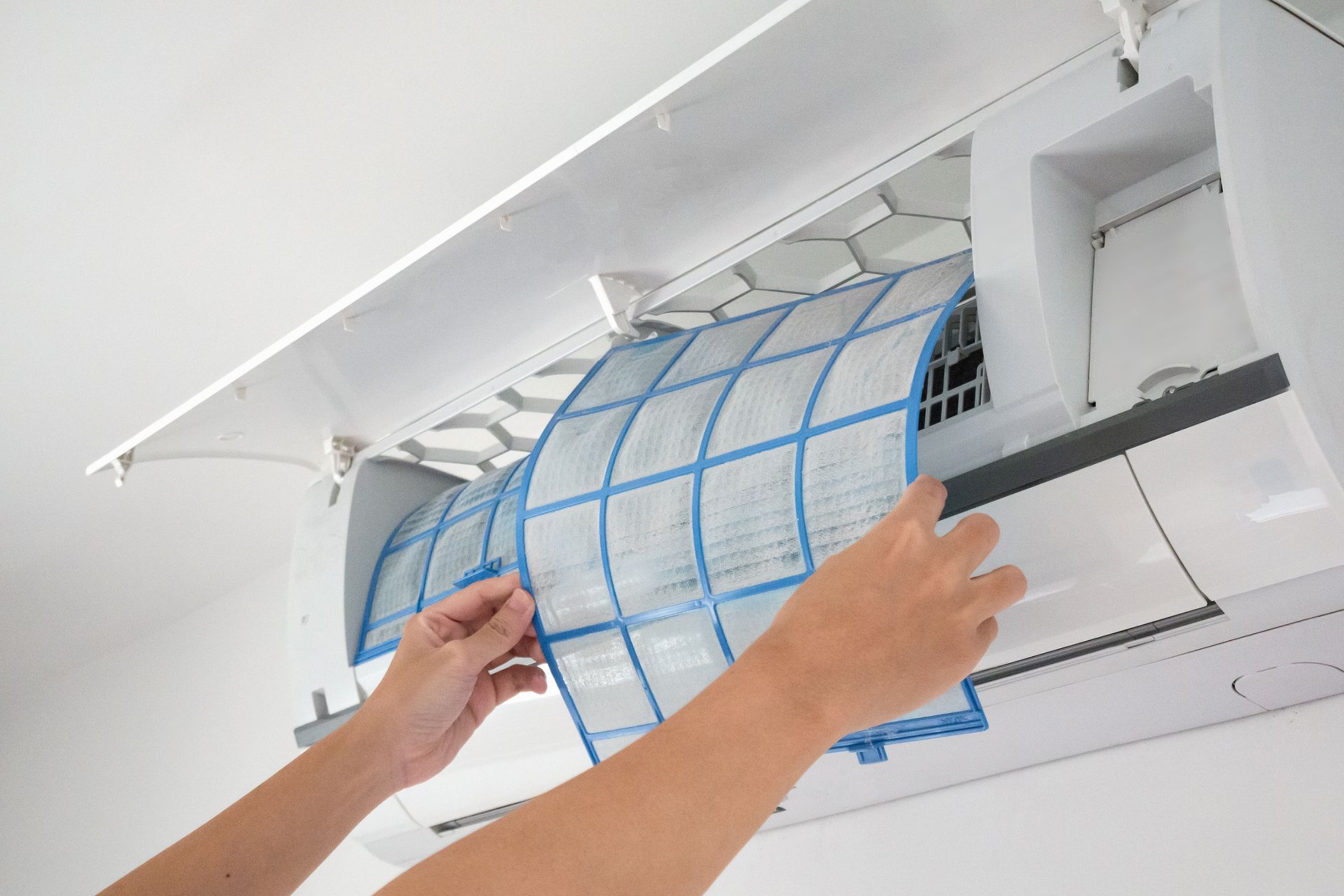 Person removing air filter from a white air conditioning unit.