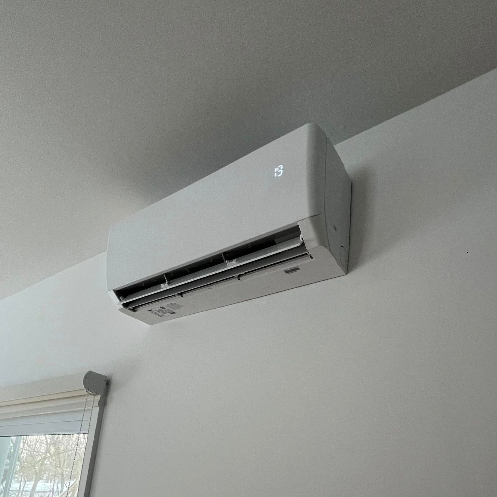 Un climatiseur blanc est monté sur un mur blanc à côté d'une fenêtre.