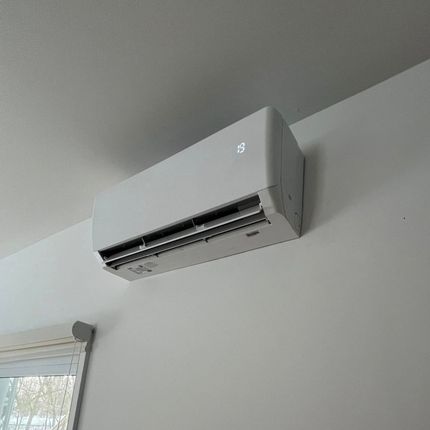 Un climatiseur blanc est monté sur un mur blanc à côté d'une fenêtre.