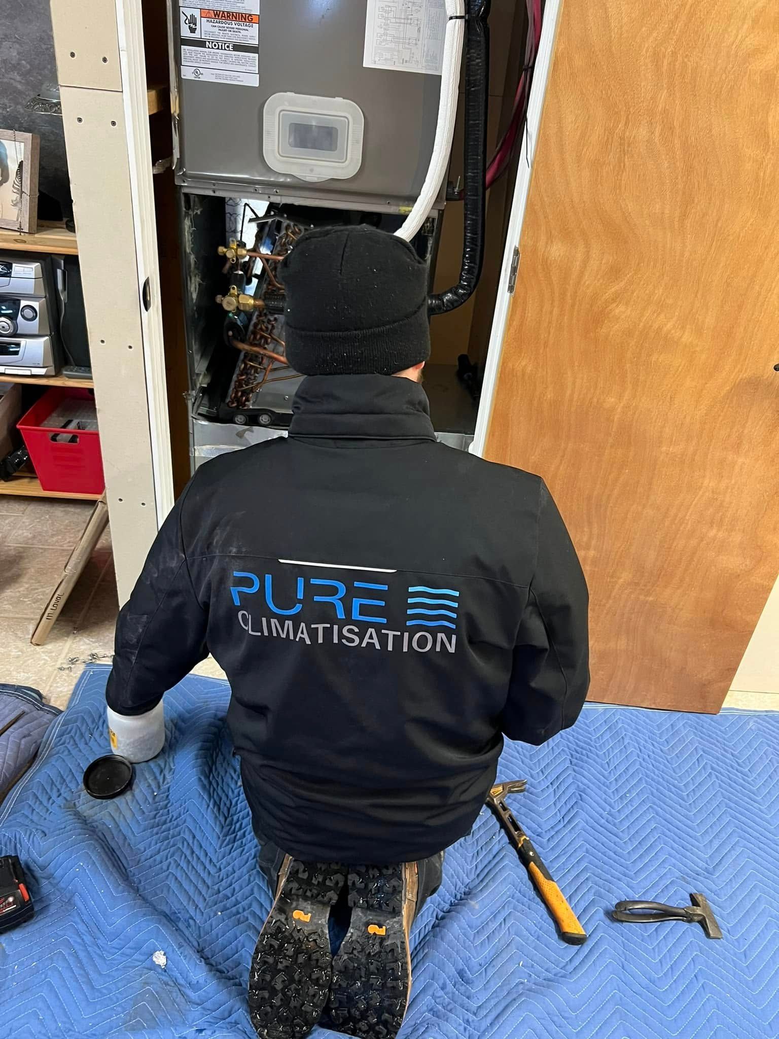Un réparateur de Pure Climatisation est agenouillé devant un climatiseur.